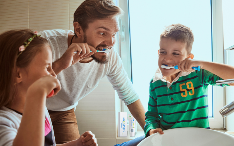 Family (man, son, daughter) around sink brushing teeth using hydroxyapatite toothpaste from Myospots.