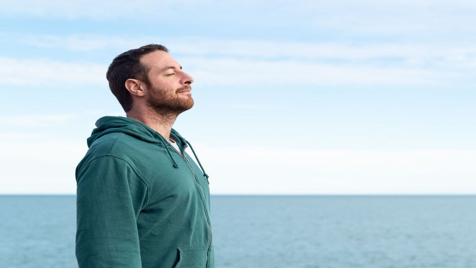 Nose breathing vs mouth breathing featured image - man standing breathing through his nose, expressing comfort, ocean backdrop.