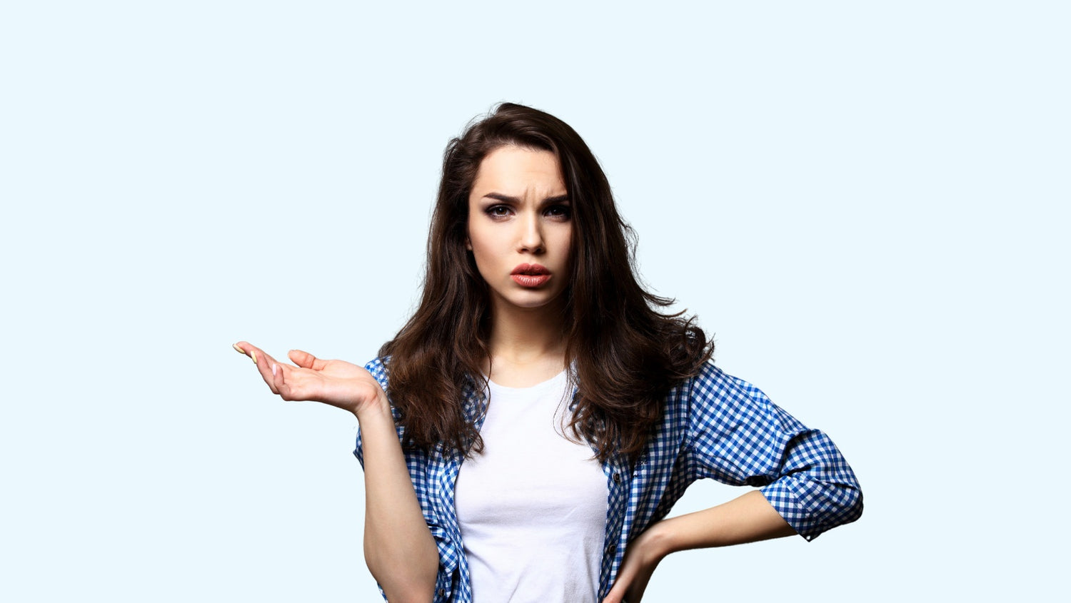 Woman looking at camera with a questioning look on her face. She has one hand on side, and the other hand raised out next to her shoulder with her palm facing upwards.