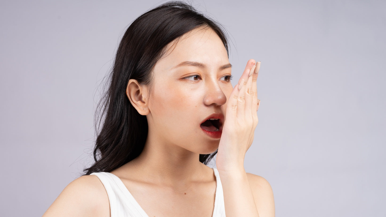 Person holding hand in front of face. She is breathing into it, smelling her own breath.